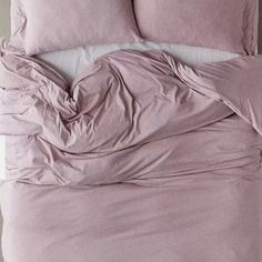 an unmade bed with pink sheets and pillows