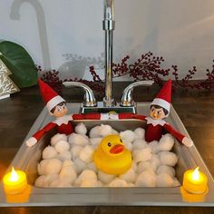 two elfs sitting in a sink with soap bubbles and a rubber ducky toy