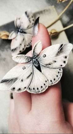 two white butterflies sitting on top of a persons finger in front of a box with other items