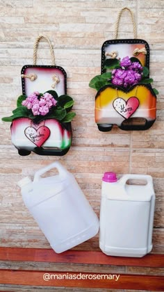 two plastic containers with flowers and hearts on them are hanging from the wall next to a white jug