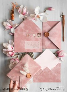 pink envelopes with white flowers and wax stamp on them, surrounded by other items