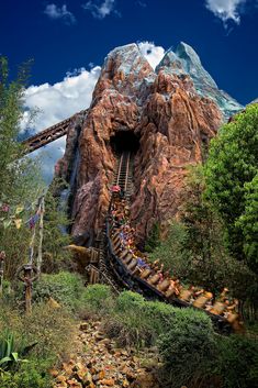 a roller coaster going down a mountain with many people on it's sides and in the middle