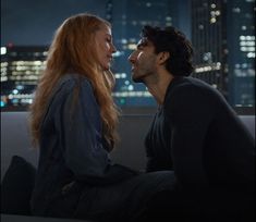 a man sitting next to a woman on top of a couch in front of a city skyline