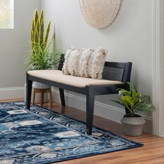 a bench with pillows on it next to a rug and potted plant in the corner