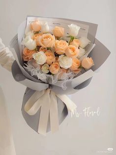 a bouquet of white and peach roses is wrapped in gray paper