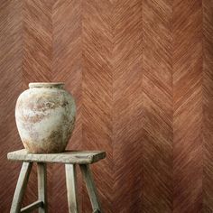 an old vase sitting on top of a wooden stool in front of a red wall