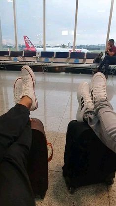 two people with their feet on luggage at an airport, one is laying down and the other is standing up