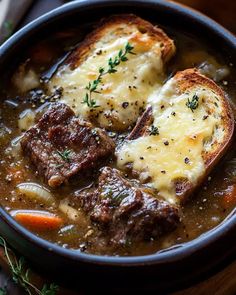 a bowl filled with meat and cheese soup on top of a wooden table next to bread