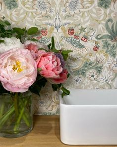 some pink and white flowers in a vase on a table next to a wallpaper