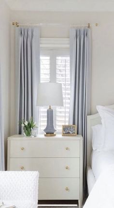 a bedroom with white bedding and gray drapes on the windowsill, along with a dresser