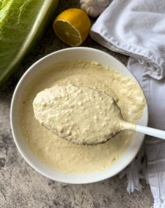 a white bowl filled with dressing next to lettuce and lemons