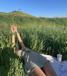 a woman laying on top of a lush green field next to a tall grass covered hillside