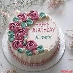 a birthday cake with pink and green frosting is on a table next to flowers