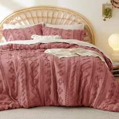 a bed with pink comforter and pillows in a room next to a wicker headboard