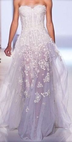 a woman is walking down the runway wearing a white dress with flowers on it's skirt