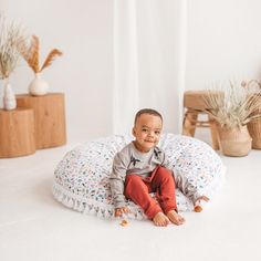 a baby sitting on a round pillow in the middle of a room with white walls