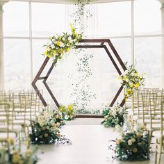 an indoor ceremony setup with flowers and greenery on the aisle, in front of a large window