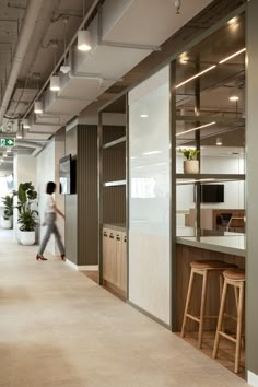 a woman walking through an office lobby with lots of counter space and plants on the walls