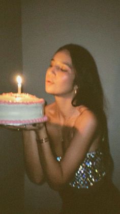 a woman holding a cake with a lit candle on it in front of her face