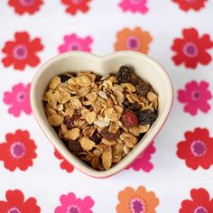 a heart shaped bowl filled with granola on top of a flowery tablecloth