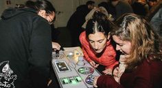 three girls looking at an electronic device on display in a room full of other people