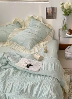 an unmade bed with blue sheets and white flowers on the side table next to it