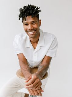 a man with dreadlocks sitting on top of a stool smiling at the camera