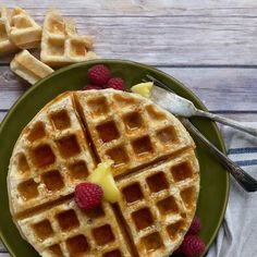 two waffles on a green plate with raspberries and butter next to them