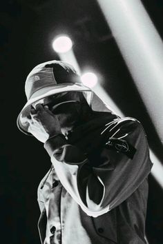 a man in a hat and trench coat standing on stage with his hands to his face