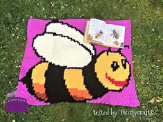 a knitted blanket with a bee on it and a book laying next to it