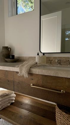 towels are stacked on the counter in front of a mirror and sink with a vase