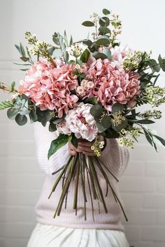 a woman holding a bouquet of pink flowers in her hands and wearing a white sweater