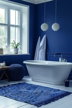 a white bath tub sitting next to a window in a blue bathroom with rugs on the floor