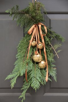 a christmas wreath hanging on the front door with bells and pine cones tied to it