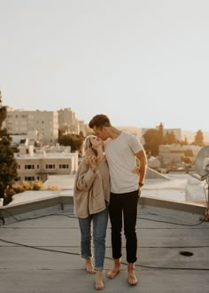 a man and woman standing on top of a roof next to each other with buildings in the background