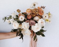 a woman holding a bouquet of flowers in her hand with white and peach colors on it