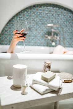 a woman holding a glass of wine in front of a bathtub with white towels