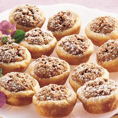 a white plate topped with mini cupcakes covered in powdered sugar and sprinkled with pink flowers