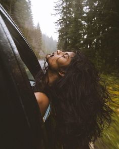 a woman is looking out the window of a car in the rain, with her hair blowing back