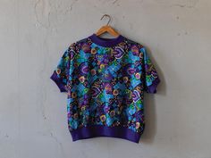 60s vintage abstract purple paisley print graphic top w/ rib accents. Great colors/shape. Nice vintage condition with wear thats consistent with age. Please see photos for reference.   Shoulder 27" Pit to pit 26" Length 23" Sleeve 33" Across Fitted Printed Purple Tops, Retro Purple Crew Neck Top, Purple Printed Cotton Tops, Vintage Patterned Crew Neck Tops, Vintage Short Sleeve Tops With Vibrant Print, Vintage Crew Neck Patterned Tops, Retro Purple Short Sleeve Top, Retro Patterned Tops With Vibrant Print, Retro Purple Tops With Graphic Print