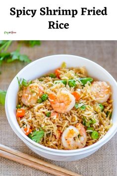 a white bowl filled with shrimp fried rice next to chopsticks and cilantro