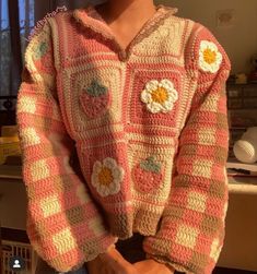 a woman wearing a pink and white crocheted sweater with flowers on the front