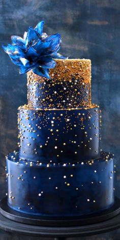 a blue and gold wedding cake on a black stand with confetti sprinkles