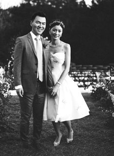 a man and woman standing next to each other in front of some flowers on the grass