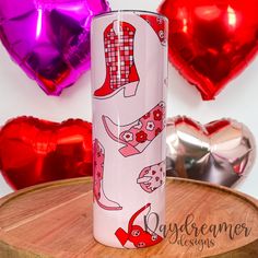 a pink tumbler sitting on top of a wooden table next to heart shaped balloons