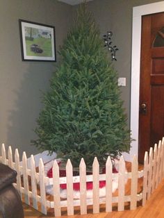 a small christmas tree is in the middle of a room with a white picket fence