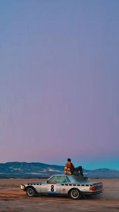 a man sitting on top of a car in the desert