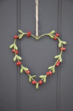 a heart shaped wreath with berries and leaves hanging on the front door's side