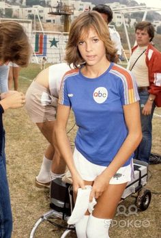 a woman in blue shirt and white shorts holding a tennis racquet next to other people