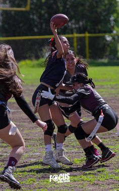 a group of young women playing a game of frisbee on a field with trees in the background